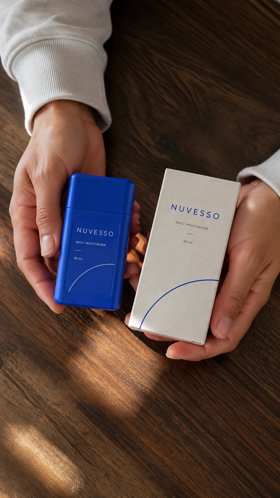 Hands presenting NUVESSO packaging on a walnut table